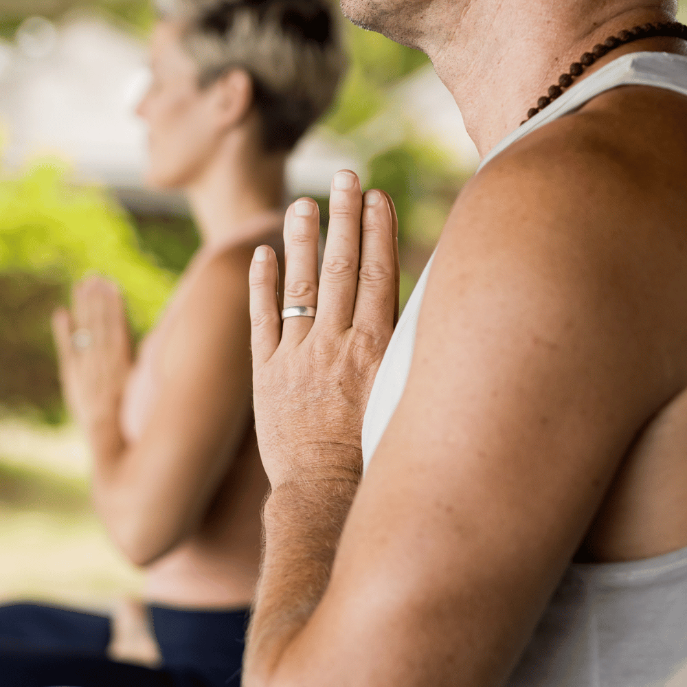 Two people practicing yoga in byron bay with a focus on their hands.